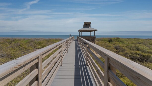 A wooden boardwalk leading to a gazebo with a slanted roof, surrounded by grassy dunes and a clear blue sky. - 2952 - Davis - Coastal Condo in Duck Steps from the Beach (Duck)