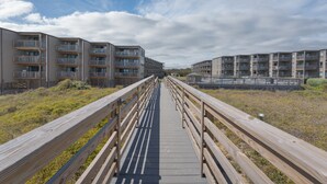 A wooden boardwalk leading to a row of modern apartment buildings with balconies. - 2952 - Davis - Coastal Condo in Duck Steps from the Beach (Duck)