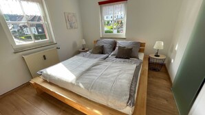 Ein Schlafzimmer mit einem Bett, zwei Nachttischen, einer Heizung und Fenstern mit Vorhängen.