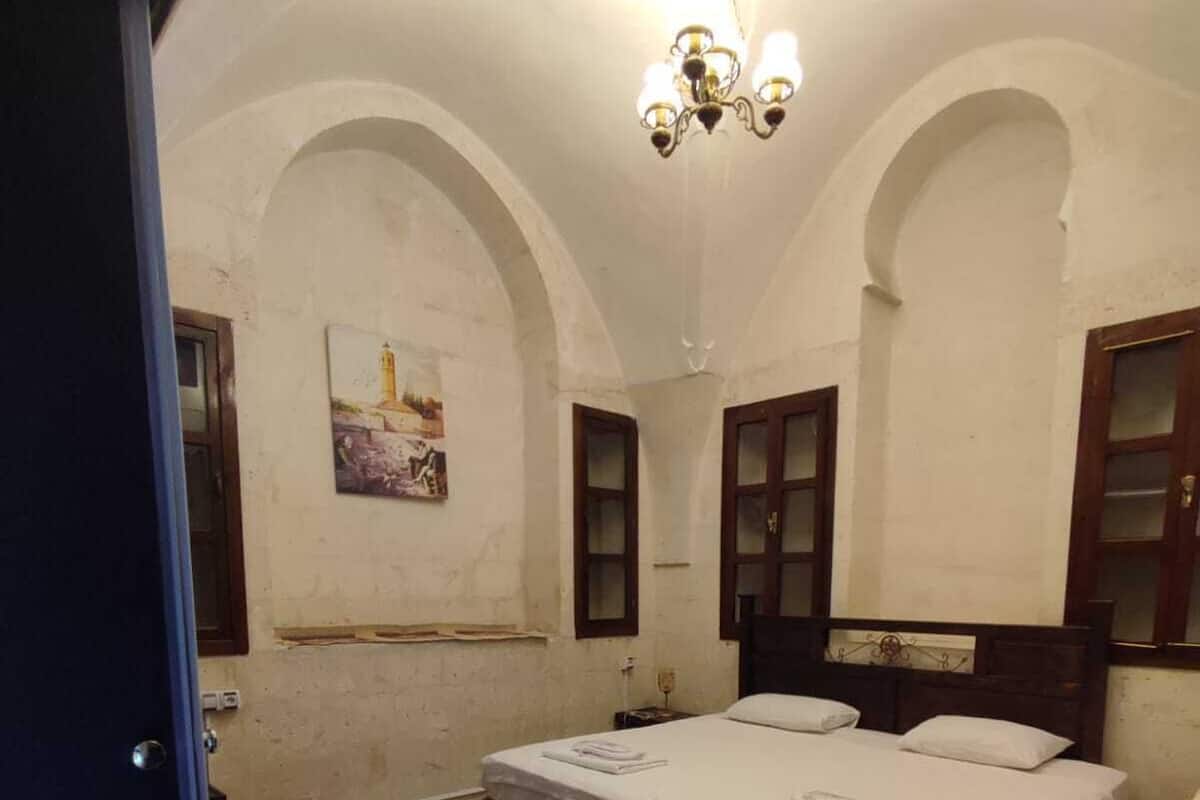 A room with a large bed, wooden flooring, and a chandelier.