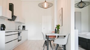 A modern kitchen with white cabinets, a coffee machine, and a dining area with a table and chairs. - Apartment 2 Teefabrik - Living at the Norder Tief (Lorup)