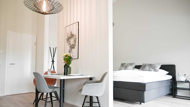 A modern room with a dining area featuring a white table, two grey chairs, and a hanging light fixture. - Apartment 2 Teefabrik - Living at the Norder Tief (Lorup)