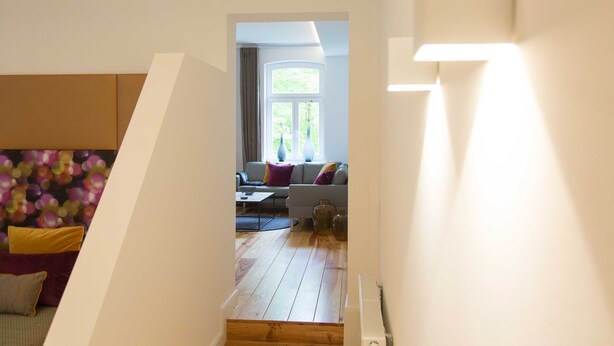 Un escalier menant à un espace de vie comprenant un canapé, des coussins, une fenêtre et un vase.