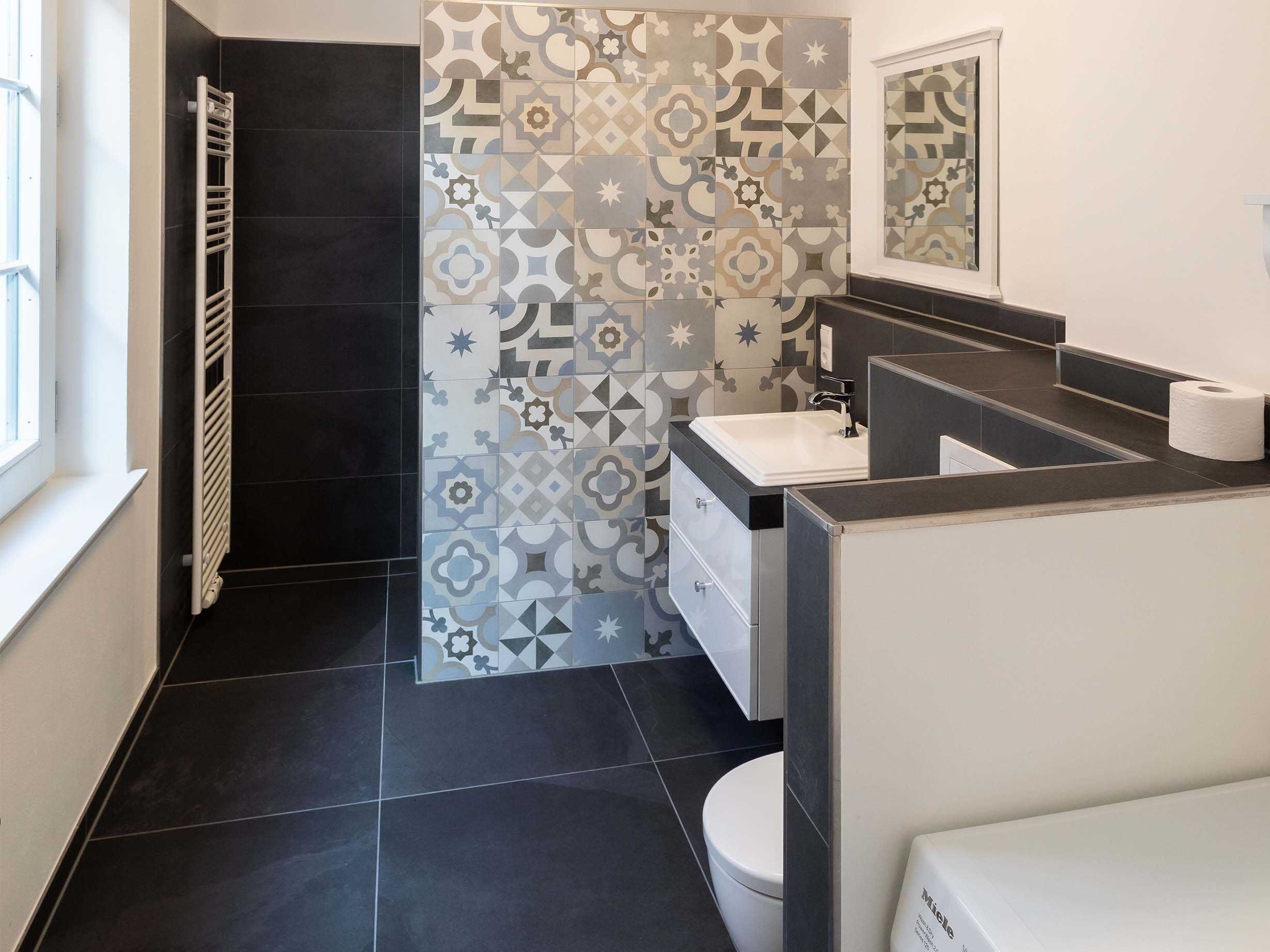 Un baño moderno con piso de baldosas blanco y negro, zona de ducha, lavamanos con espejo y retrete.