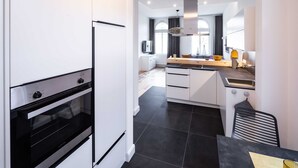 A modern kitchen with white cabinetry, a built-in oven, and a dining area with a wooden table and chairs. - Apartment 4 Wohnen am Schloss - Living at Schloßplatz (Oldenburg)