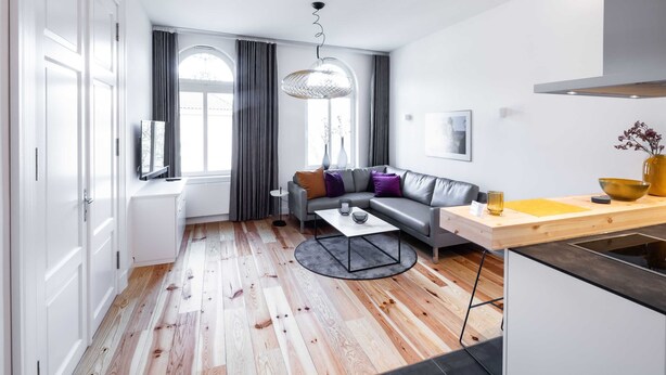 A modern living room with a grey sofa, a coffee table, and a wooden dining table. - Apartment 4 Wohnen am Schloss - Living at Schloßplatz (Oldenburg)