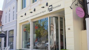 A building with a large window displaying a car and a tree. There is a sign with the text "fm" and "Büromöbel" on the window. - Apartment 4 Wohnen am Schloss - Living at Schloßplatz (Oldenburg)