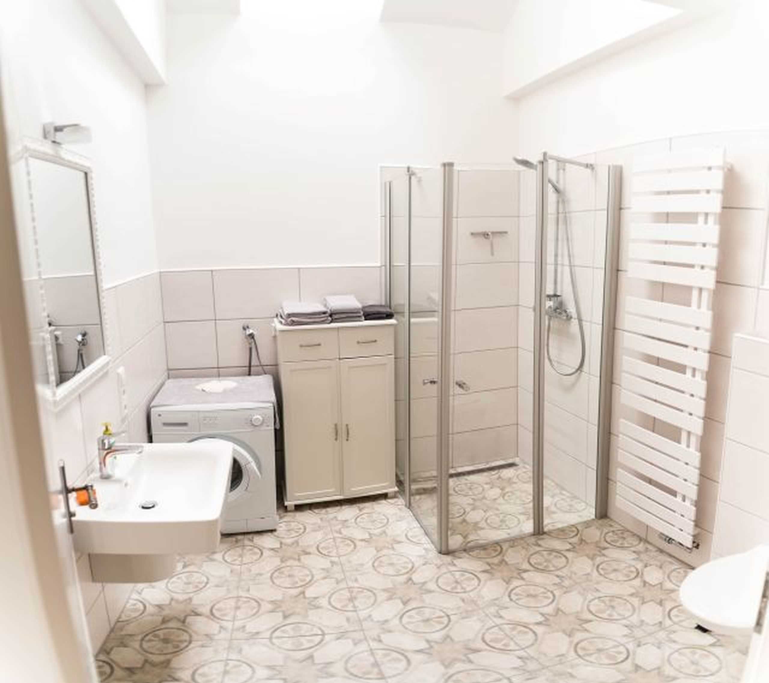 Un baño con ducha, lavamanos, lavadora y un armario.
