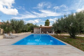 A rectangular swimming pool with a tiled deck, surrounded by olive trees and a stone wall. - Villa Bartolomeo with Pool, Garden and Wi-Fi (Modica)