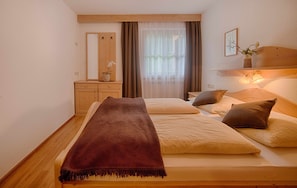 Quarto com duas camas, cabeceira de madeira, espelho, cômoda e janela com cortinas.