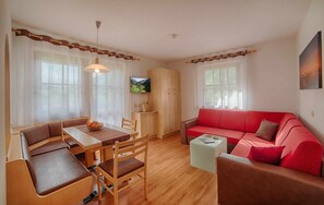 Quarto com mesa de jantar, cadeiras, sofá vermelho, televisão e um armário.