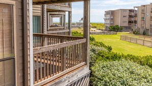 Un balcon en bois offrant une vue sur une plage et, au loin, sur un immeuble à plusieurs étages.