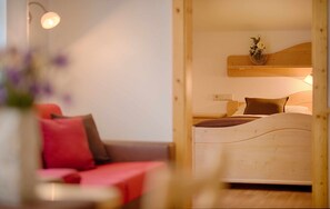 A bedroom with a wooden headboard, a bed with a brown pillow, a bedside table, and a wall-mounted shelf with flowers.
