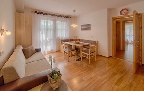 A living room with a sofa, a dining table with chairs, a wooden floor, and a door leading to another room.