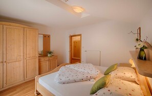 A bedroom with a bed, wooden wardrobe, a mirror, and a small table with a vase.
