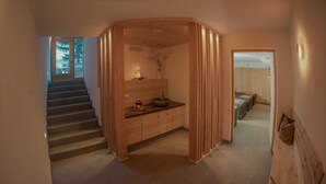 Un pasillo con una escalera de madera, un lavabo con lavamanos y vista a una habitación con cama y ventana.