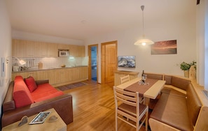 Eine moderne Küche mit Holzausstattung, ein Essbereich mit Tisch und Bänken sowie eine gemütliche Sitzecke mit einem roten Sofa.