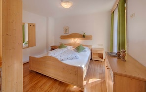 A wooden bed with pillows, a nightstand, a mirror, and a wooden dresser with a vase.