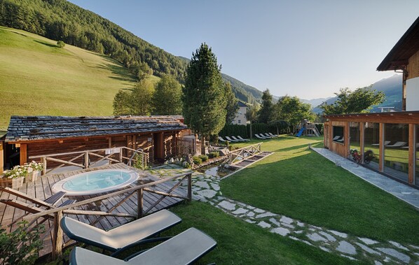 Une cabane en bois avec un jacuzzi, une cour verdoyante et une vue sur les montagnes en toile de fond.