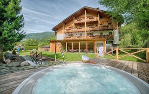 Un chalet en bois doté d’un bain à remous, d’une terrasse en bois et offrant une vue sur les montagnes.