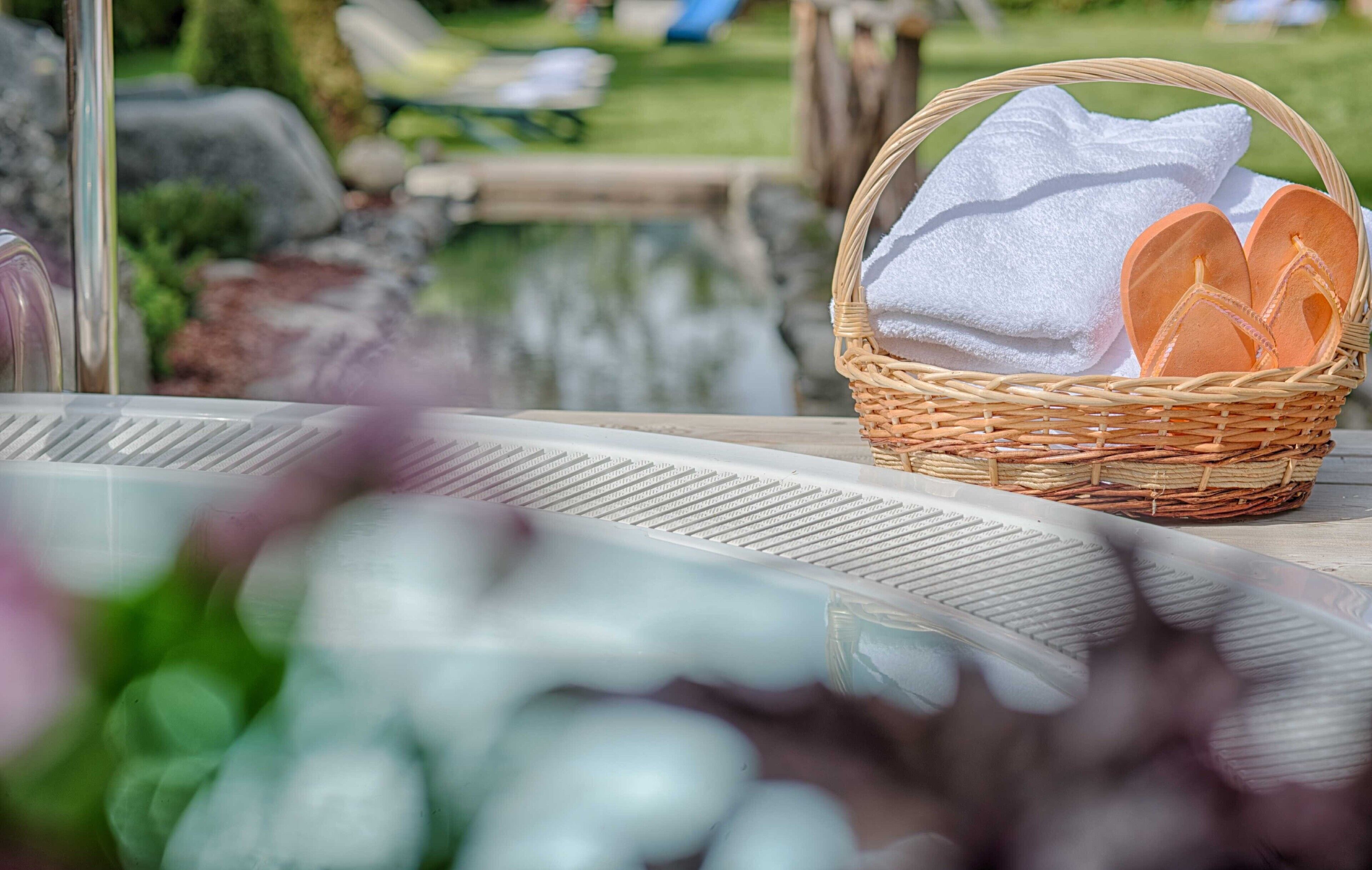 A wicker basket with towels and flip-flops on a table near a pool.