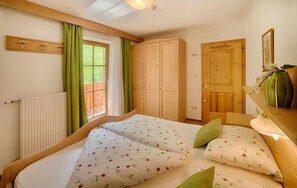 Une chambre à coucher avec un lit double, une armoire en bois, un radiateur, une fenêtre avec des rideaux et une porte.