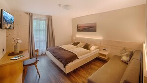 A modern hotel room with a bed, bedside table, chair, and a sofa.
