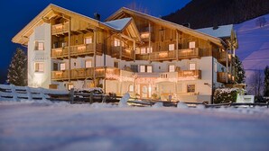 A multi-story wooden building with balconies, a sign indicating 'Appartments,' and a snowy landscape.
