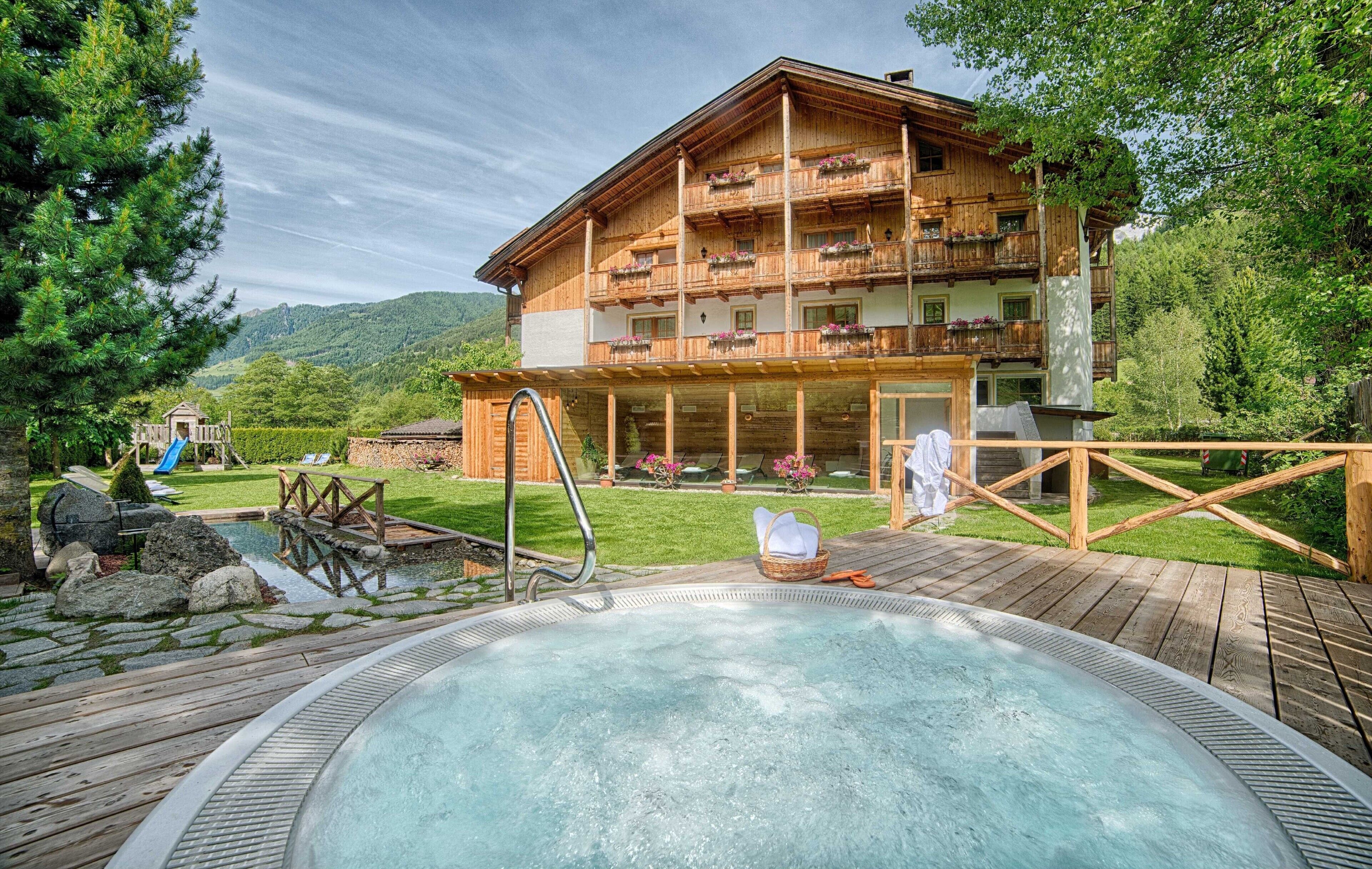 A wooden chalet with a hot tub, wooden deck, and a view of the mountains.