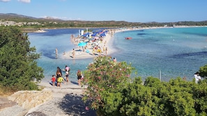 A coastal beach with clear waters, a sandy shore, and a view of the sea.