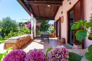 A covered patio area with a stone wall, a table with chairs, and potted plants.