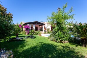 A house with a garden, a pool, and a patio with lounge chairs.