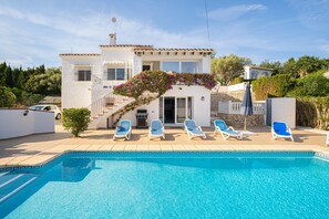 Vista de la piscina, una casa con sillones de descanso y una escalera que conduce a la entrada.