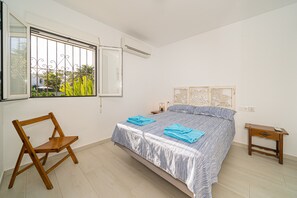 A bedroom with a bed, a wooden chair, a bedside table, and a window with a view.