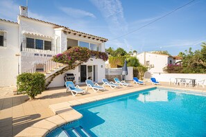 A poolside area with lounge chairs, a pool, and a building with a balcony.