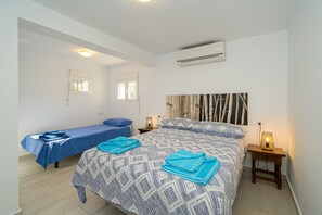 Une chambre à coucher comprenant un lit, un petit lit, deux tables de chevet, un climatiseur et deux fenêtres.