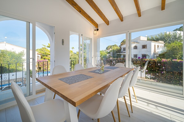 A dining area with a wooden table, white chairs, and large windows offering a view of the surrounding landscape.