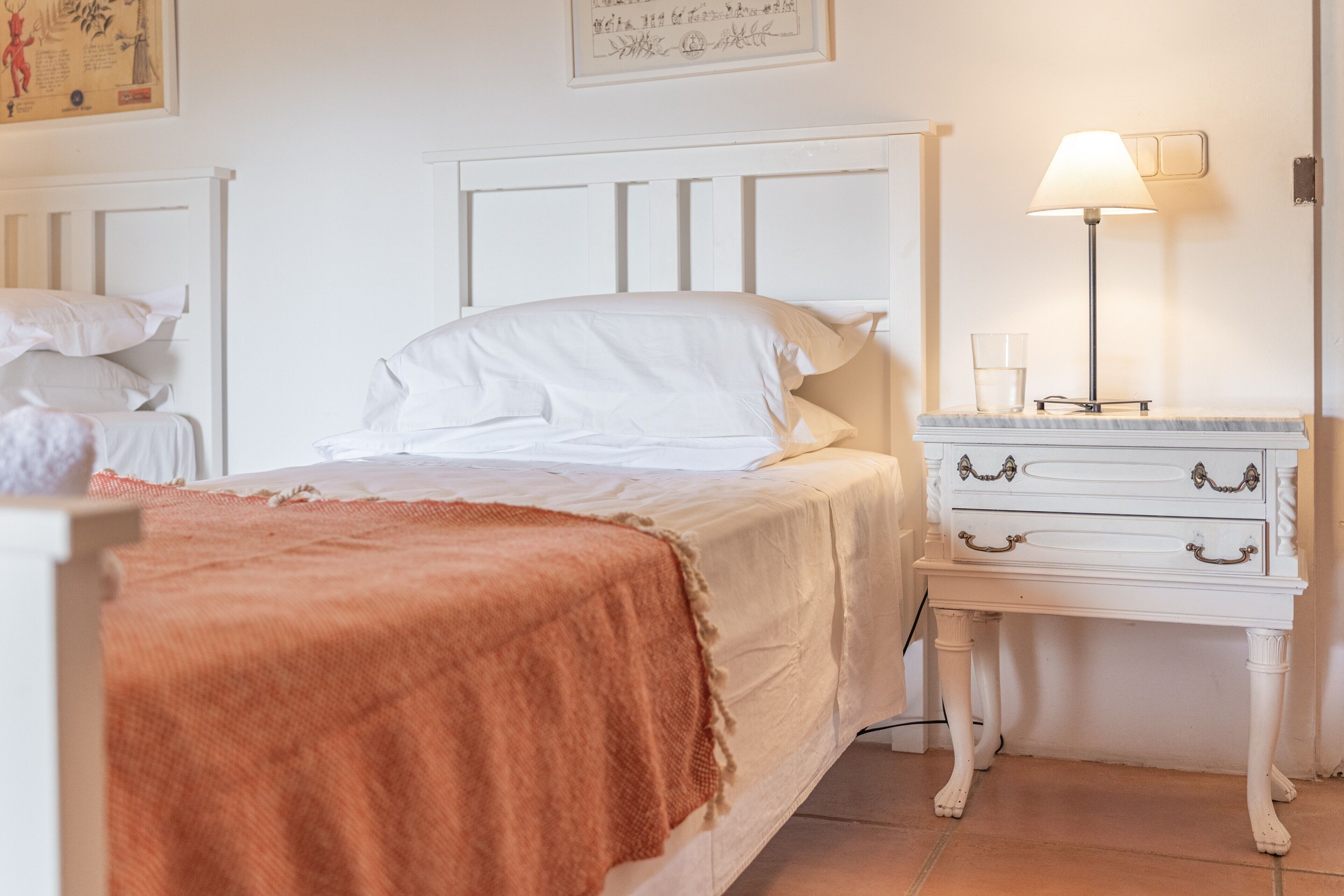 Une chambre à coucher avec un lit, une table de chevet, une lampe et un mur orné d’un tableau encadré.