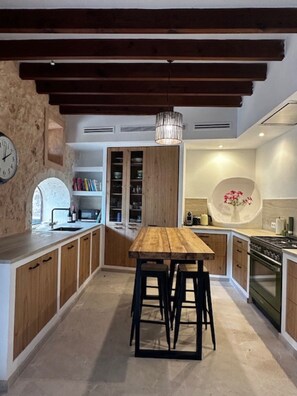A modern kitchen with wooden cabinets, a central island with stools, a built-in oven, and a clock on the wall. - Holiday Home 'Numero Uno' with Sea View, Wi-Fi and Air Conditioning (Buger)