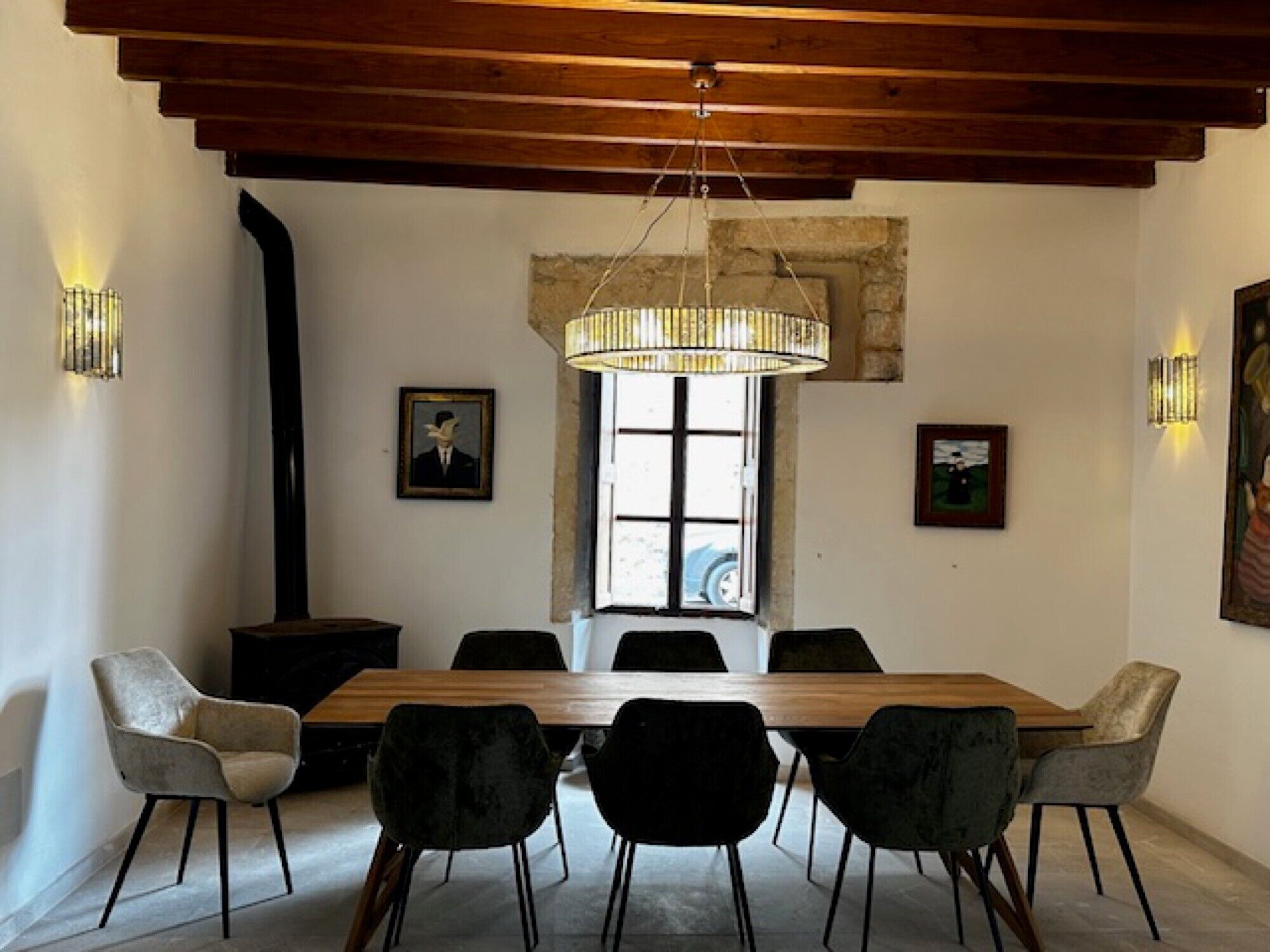 A dining area with a wooden table, six chairs, a chandelier, and artwork on the walls.