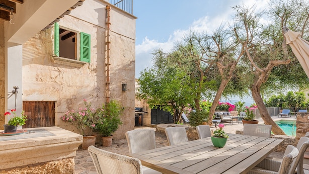 A patio with a wooden table and wicker chairs, a stone wall, and a pool in the background. - Holiday Home 'Numero Uno' with Sea View, Wi-Fi and Air Conditioning (Buger)