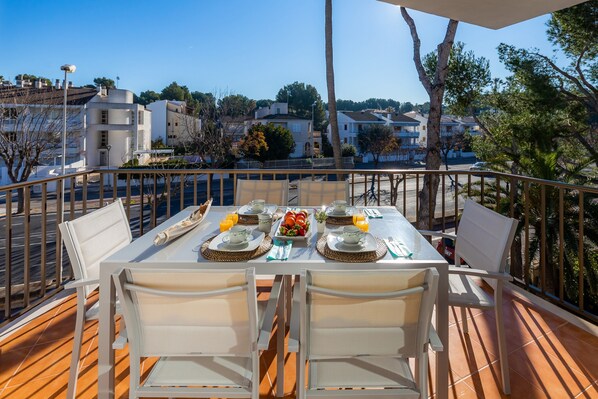 Un balcón con mesa dispuesta para el desayuno, mobiliario exterior y vistas del barrio.