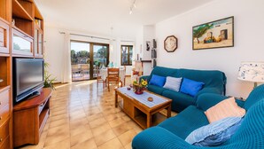 A living room with a TV, sofa, coffee table, and a dining area with chairs and a table. - La Encina Apartment with Mountain Views, Balcony, Shared Outdoor Area & Wi-Fi (Pto d'Alcudia)
