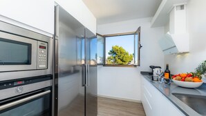 A modern kitchen with stainless steel appliances, a window with a view, and a bowl of fruit on the counter. - La Encina Apartment with Mountain Views, Balcony, Shared Outdoor Area & Wi-Fi (Pto d'Alcudia)