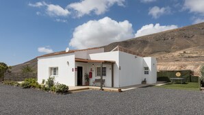 Un edificio blanco con techo de tejas, una banca y una mesa en el exterior.