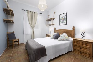 Un dormitorio con cama, mesitas de noche, una silla, lámpara colgante y estante en la pared.