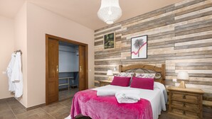 Un dormitorio con cabecera de madera, cama con ropa de cama rosa, mesita de noche con lámpara y un cuadro colgado en la pared.