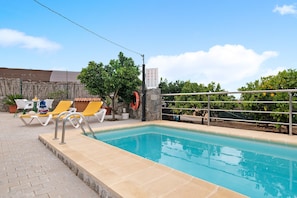 Una piscina con sillones de descanso, un flotador salvavidas y un muro de piedra.