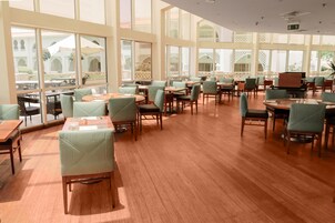 Un comedor amplio con varias mesas y sillas, y grandes ventanales que dan a un patio exterior.