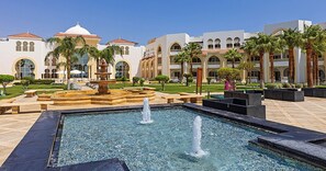 A courtyard with a fountain, palm trees, and a building with arched windows and a dome. - Old Palace Sahl Hasheseh (Sahl Hasheeh)
